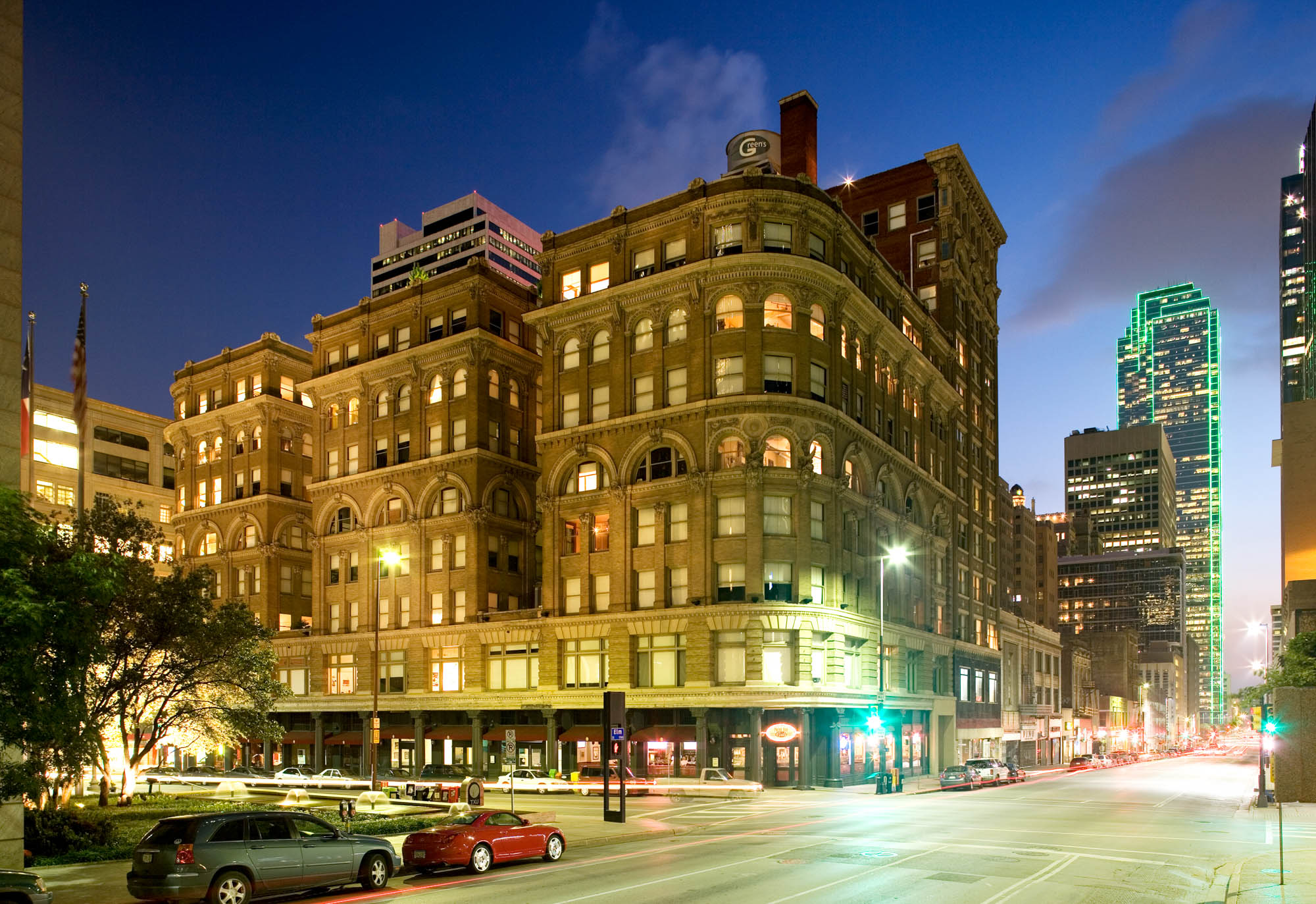 Evening, distanced street level view of The Wilson apartments at the corner of the street with all the lights turned on inside, shining out the windows