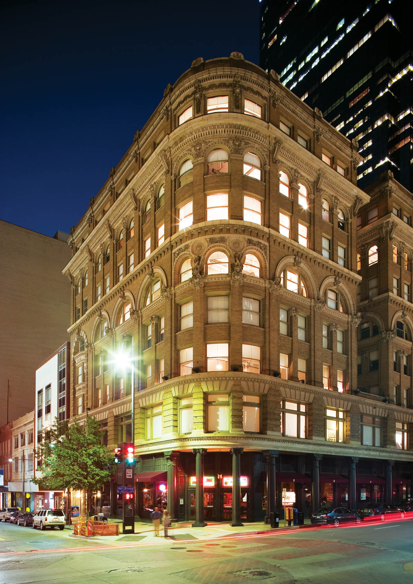 Evening street level view of The Wilson apartments at the corner of the street with all the lights turned on inside, shining out the windows