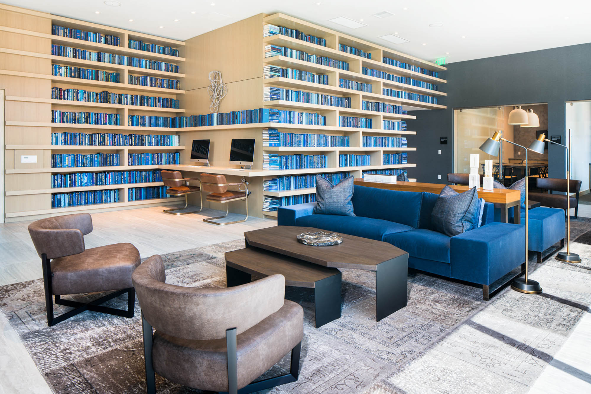 A lounge space with seating speaces, a floor to ceiling library and two computer monitors at the Atelier business center apartments in downtown la