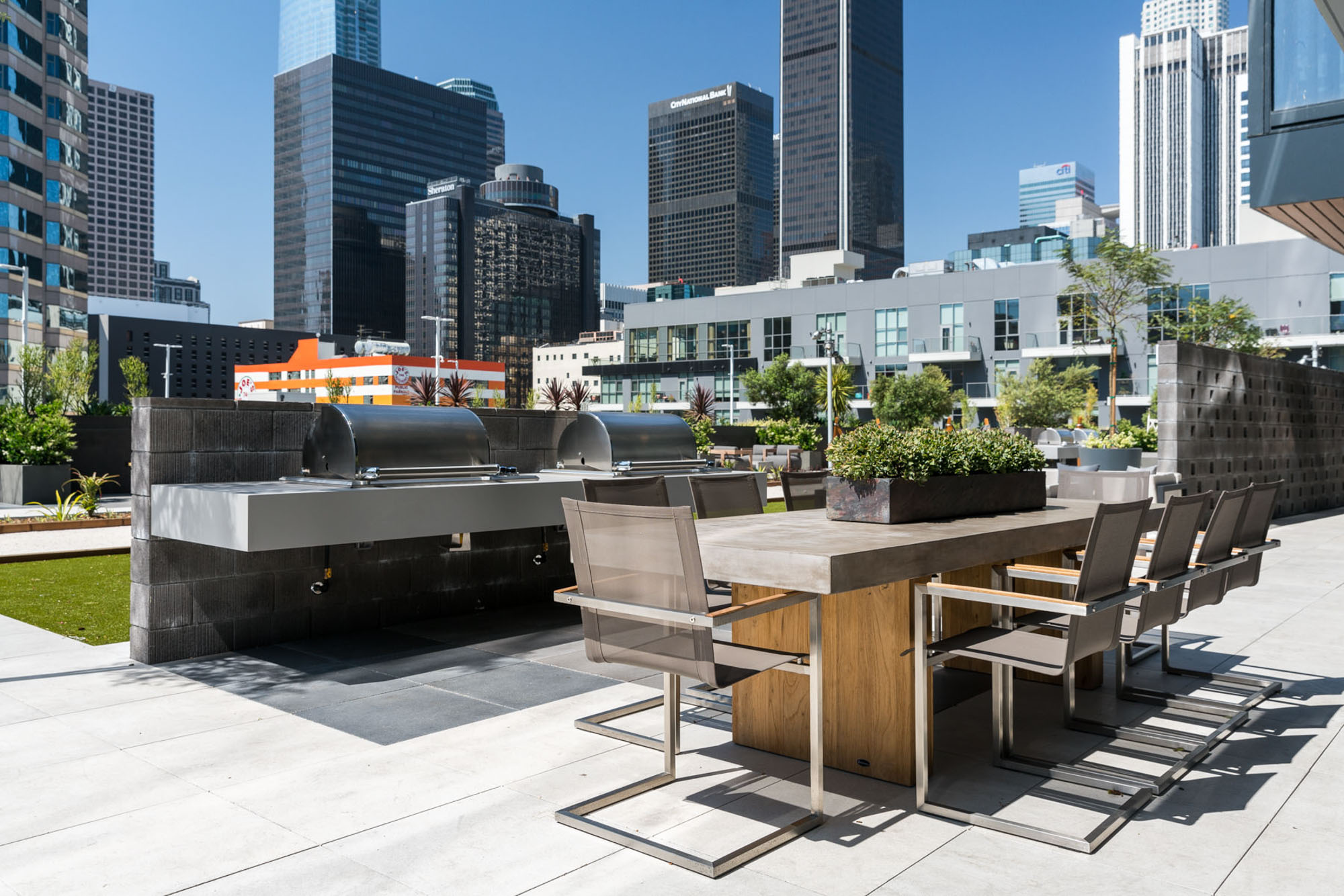 A courtyard with an outdoor grill and dining table, with city views of skyscrapers at Ateliers luxury apartments in Los Angeles