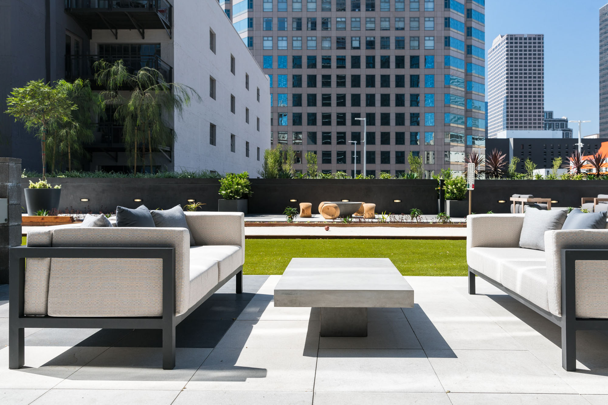 A courtyard with outdoor seating and a bocce ball court with city views of skyscrapers at Ateliers luxury apartments in Los Angeles