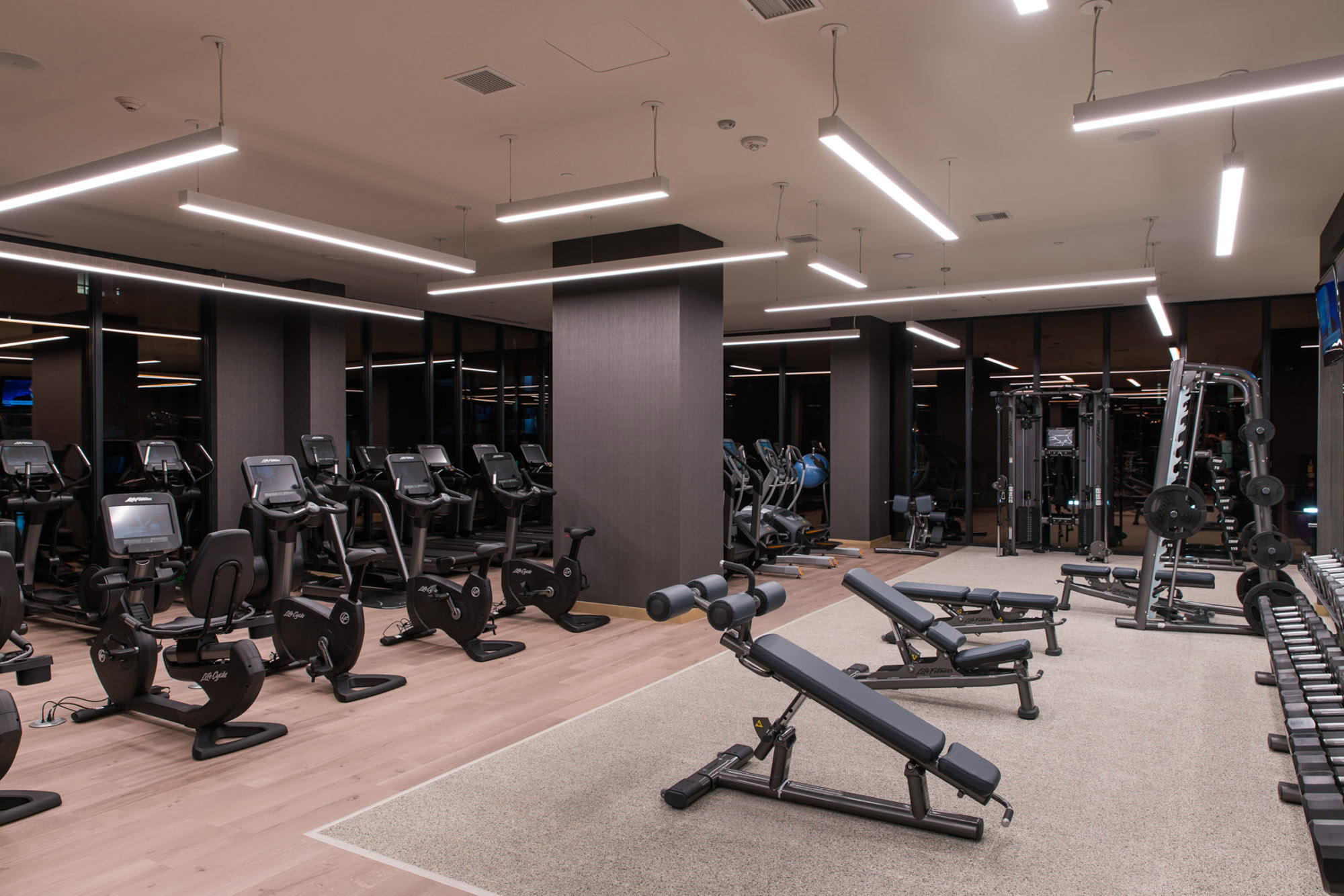 A fully equipped fitness center with weights and machines in a flourescent lit room at Ateliers luxury apartments in downtown los angeles
