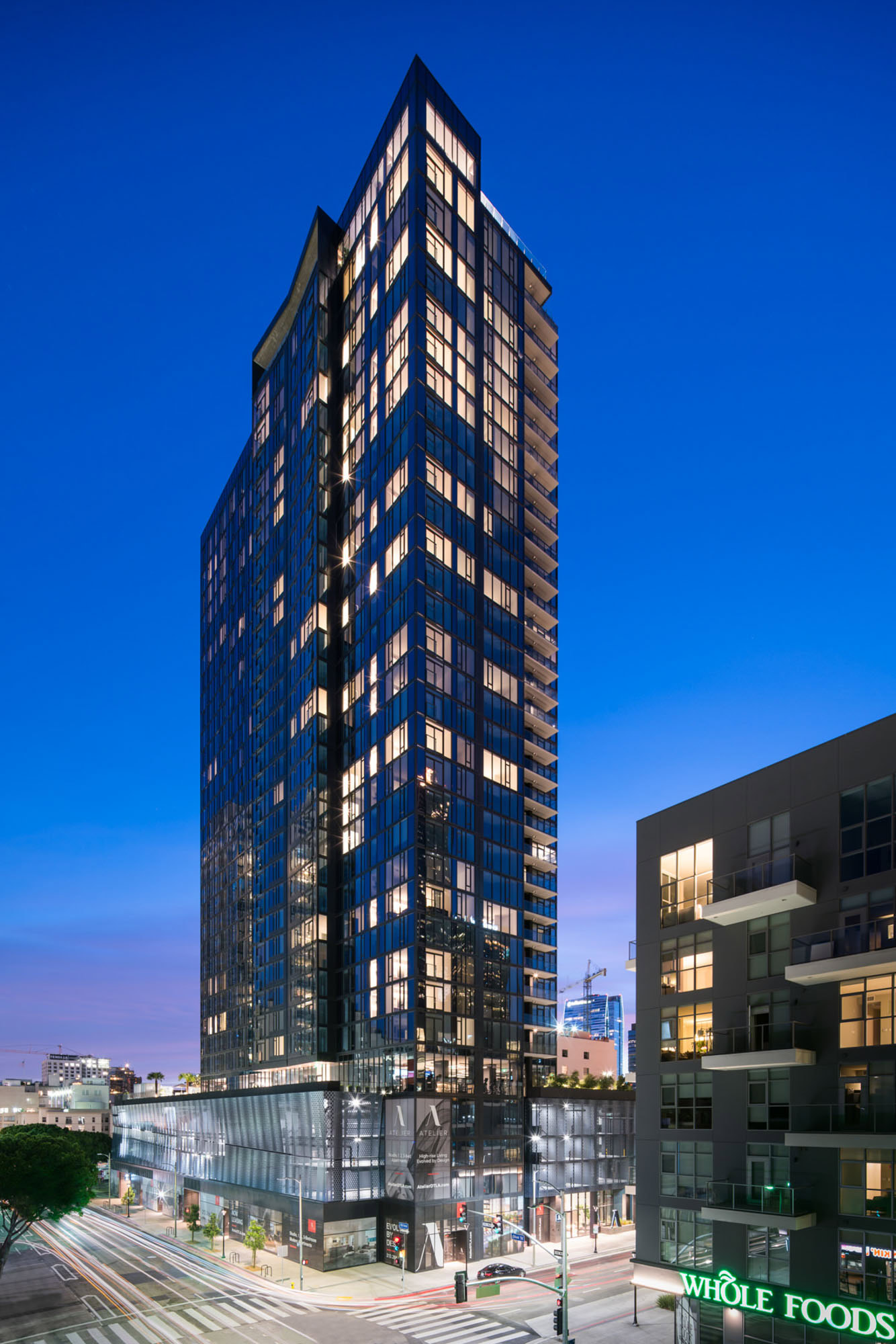 An exterior image of the Atelier apartments at twilight with bright lights shining through the apartment in downtown LA