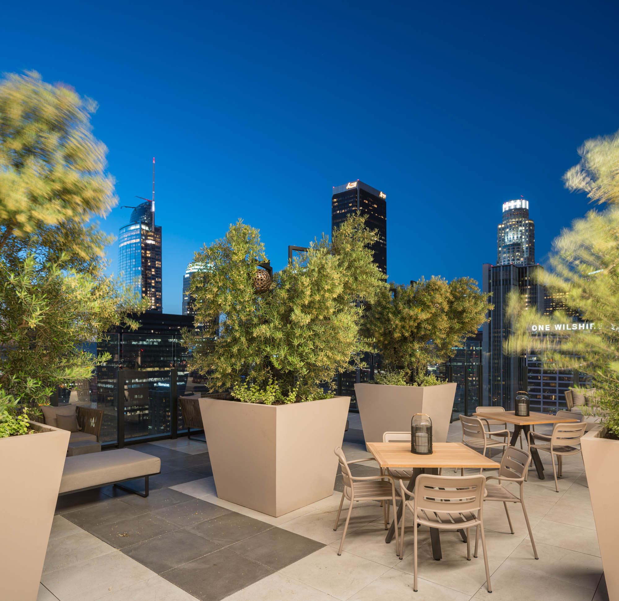A rooftop terrace with lounging chairs and an evening view of the city skyline at Ateliers luxury apartments in downtown LA