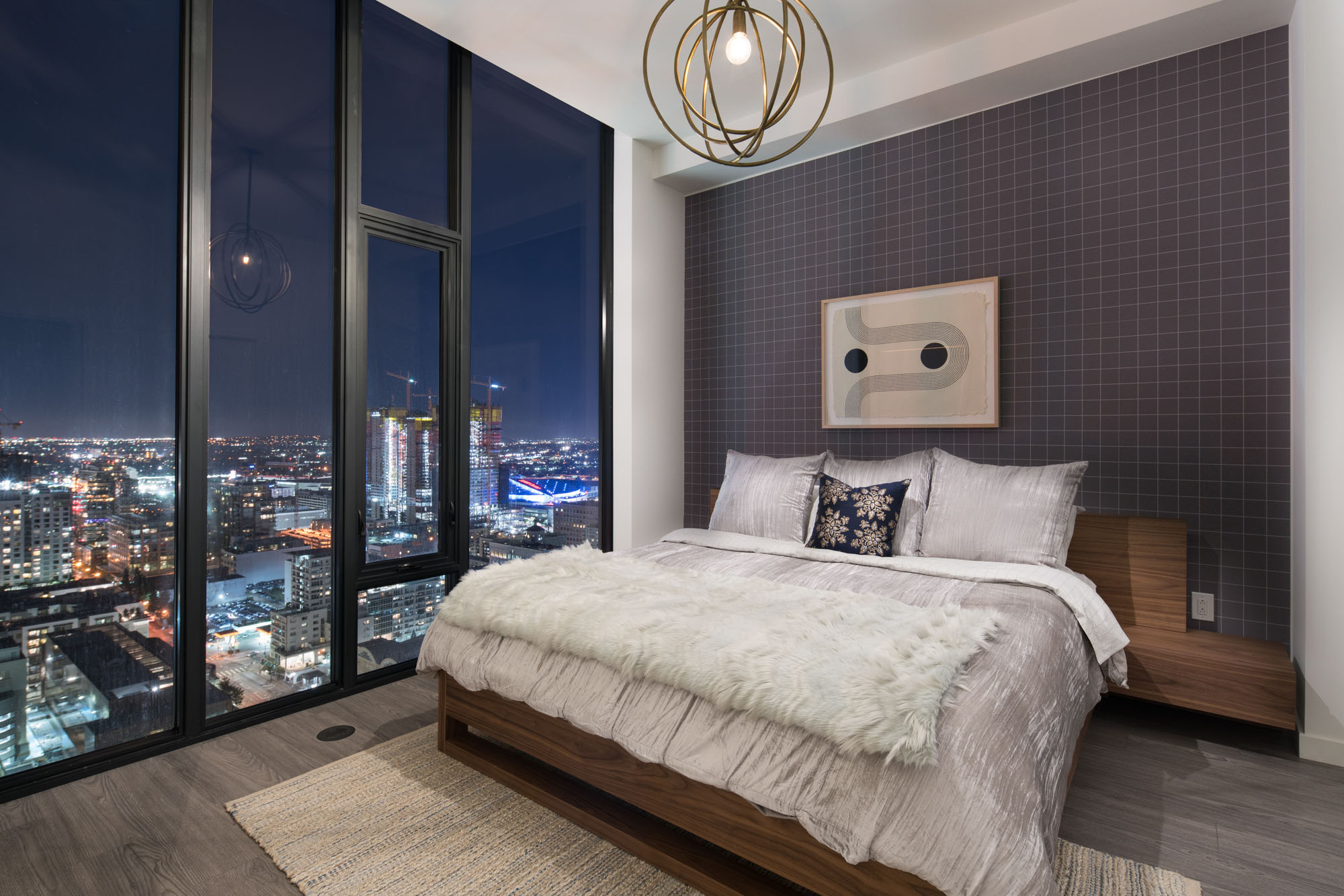 A bedroom with floor to ceiling windows showing evening city views at Ateliers luxury apartments in downtown Los Angeles