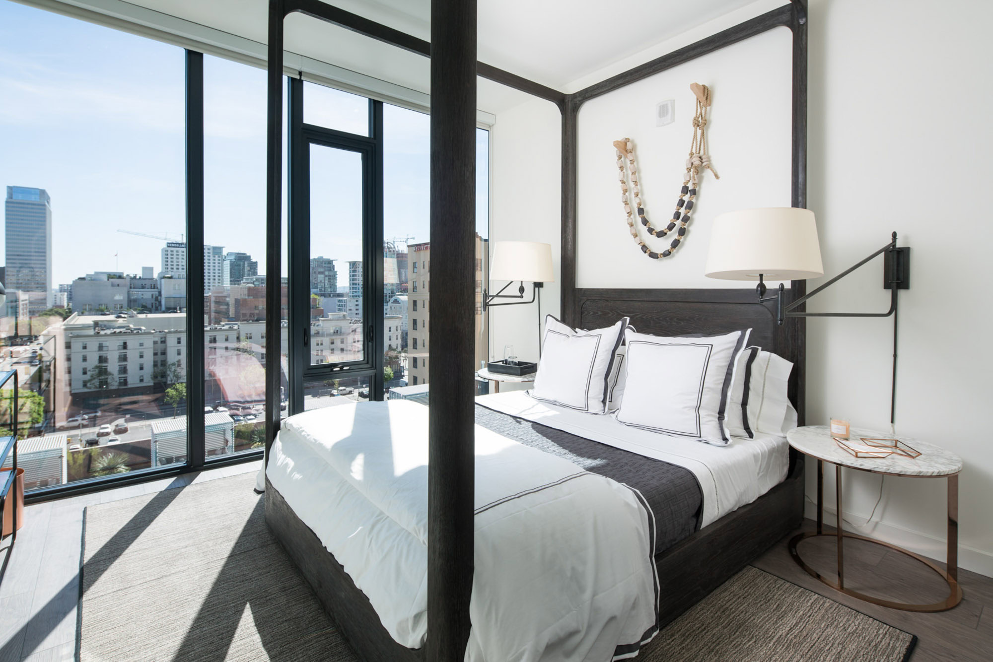 A bedroom with floor to ceiling windows showing city views at Ateliers luxury apartments in downtown Los Angeles