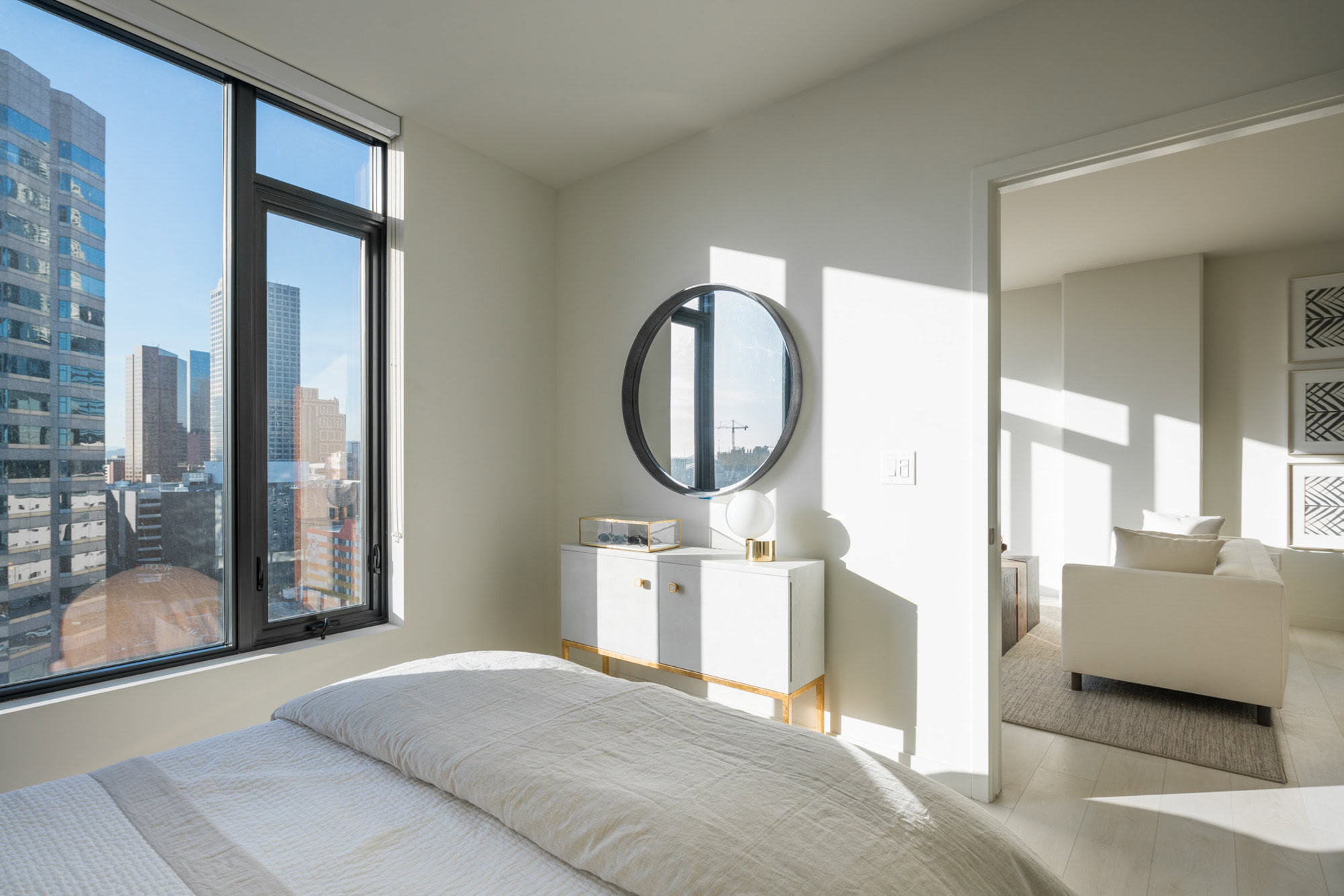 A bedroom with floor to ceiling windows and a door to the living room showing city views at Ateliers luxury apartments in downtown Los Angeles