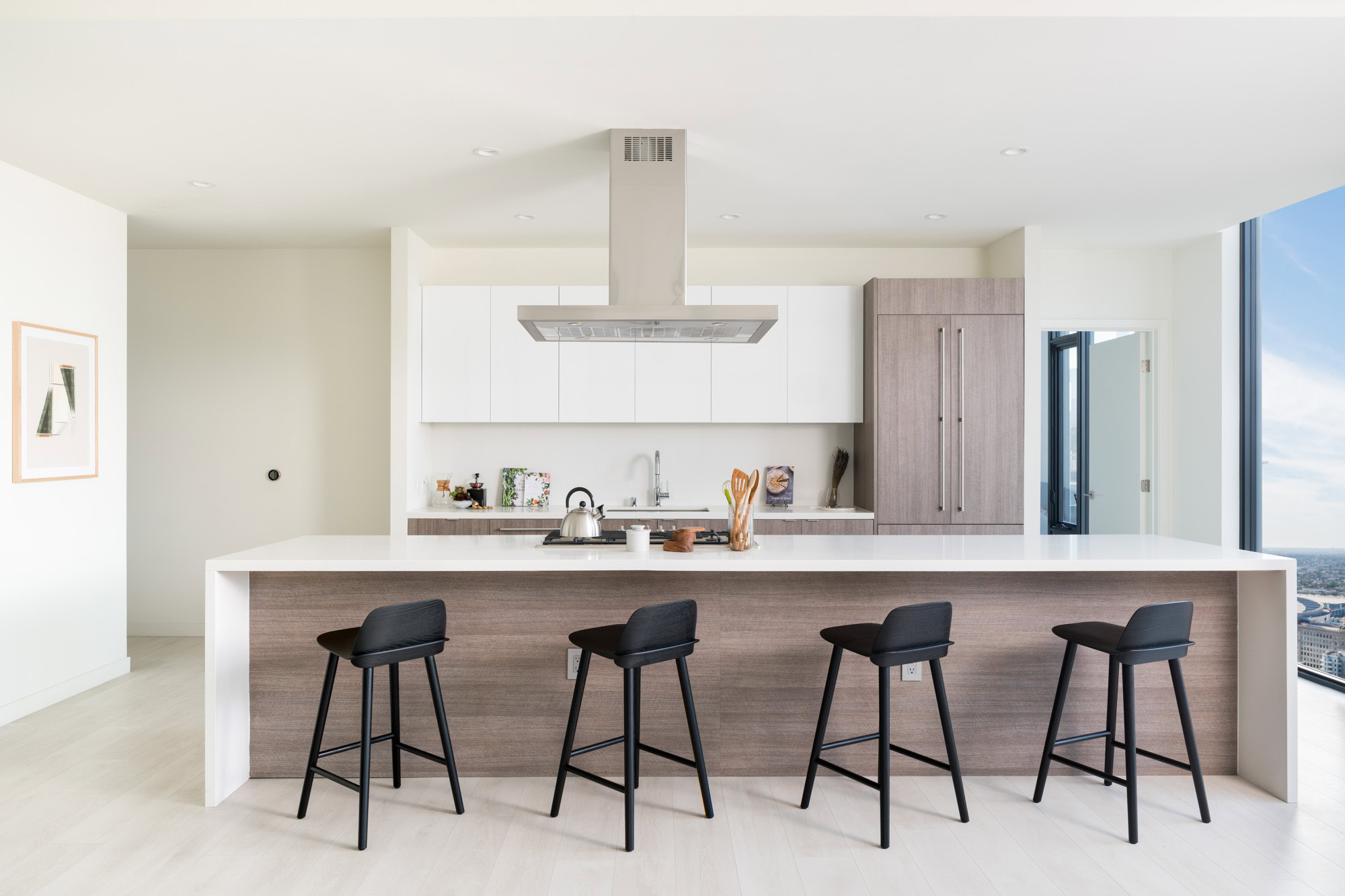 A kitchen with a kitchen island seating four and a floor to ceiling window to showing bright city views in Ateliers luxury apartments in DTLA