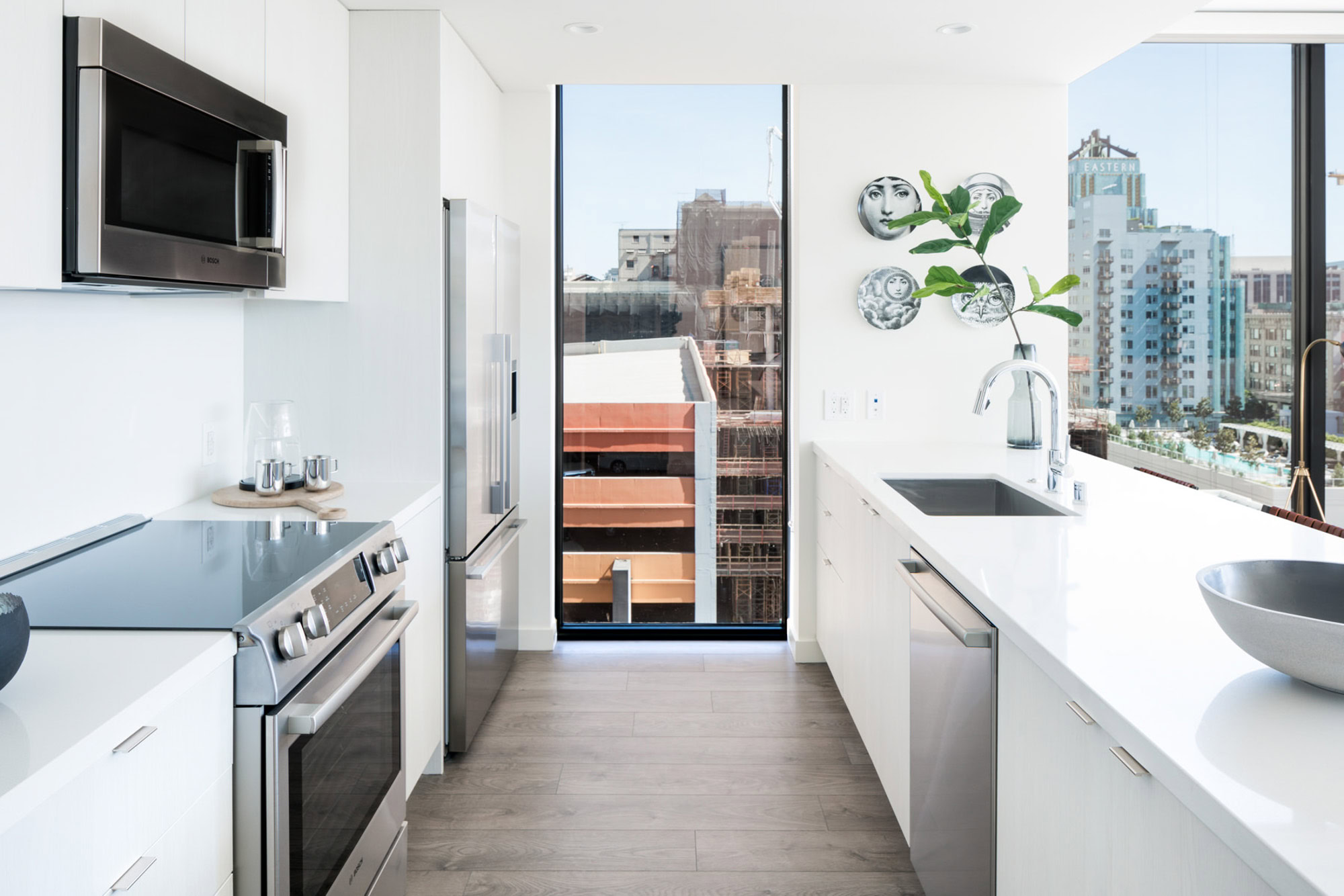 A Galley style kitchen with a glacier white quatrz backsplash and counters, stainless steel appliances and a floor to ceiling window at Ateliers luxury apartments in DTLA