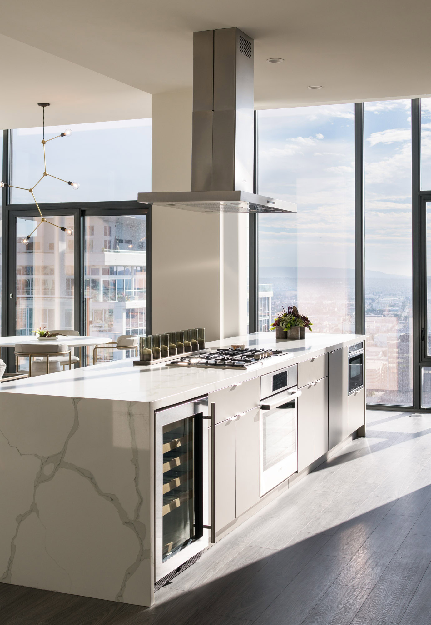 A modern luxury kitchen island with a stove next to a floor to ceiling wall showing bright city views in Ateliers DTLA high rise apartments