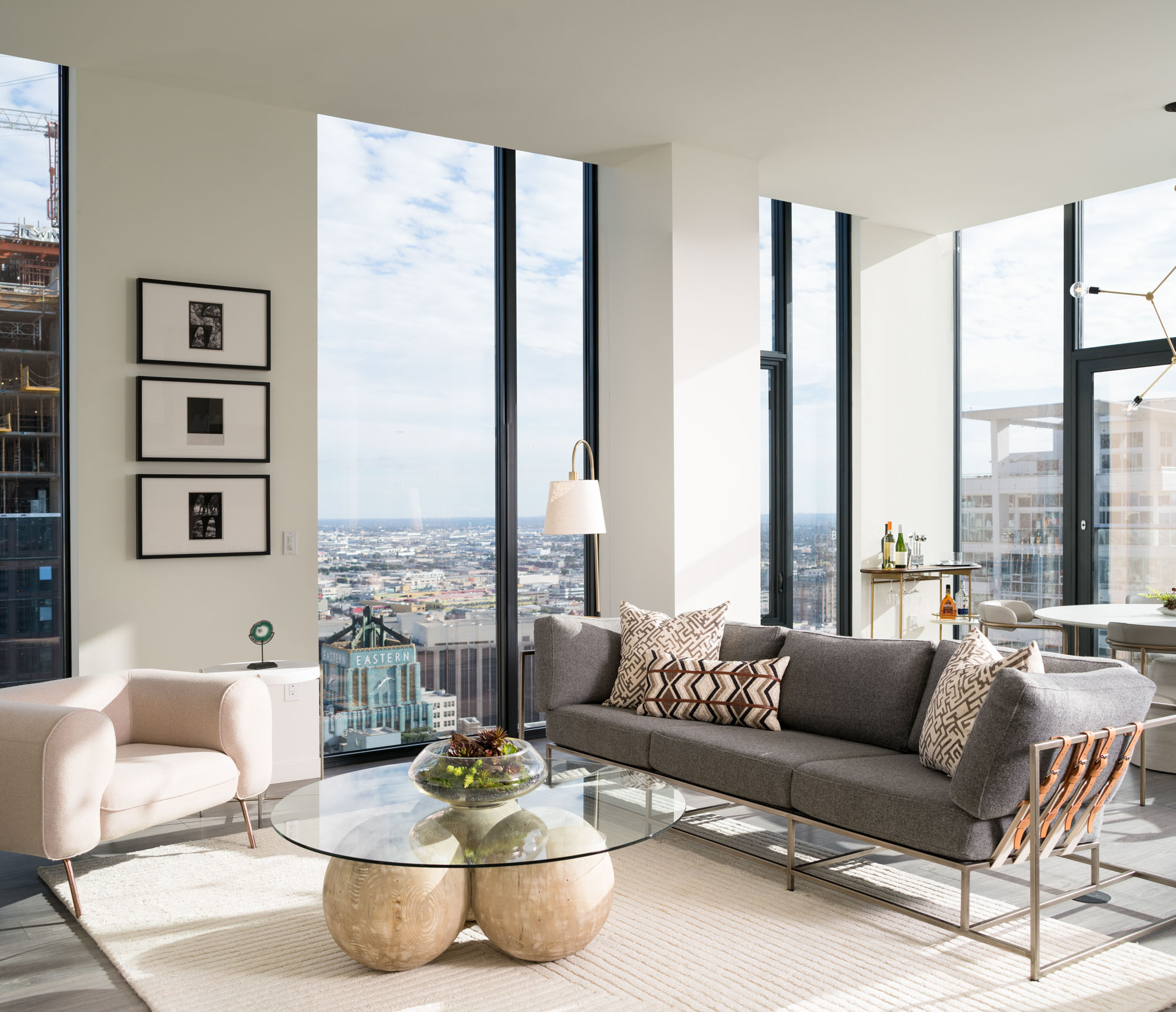 A living room with modern furniture, floor to ceiling glass walls with daytime city views in an Atelier luxury apartment in downtown LA