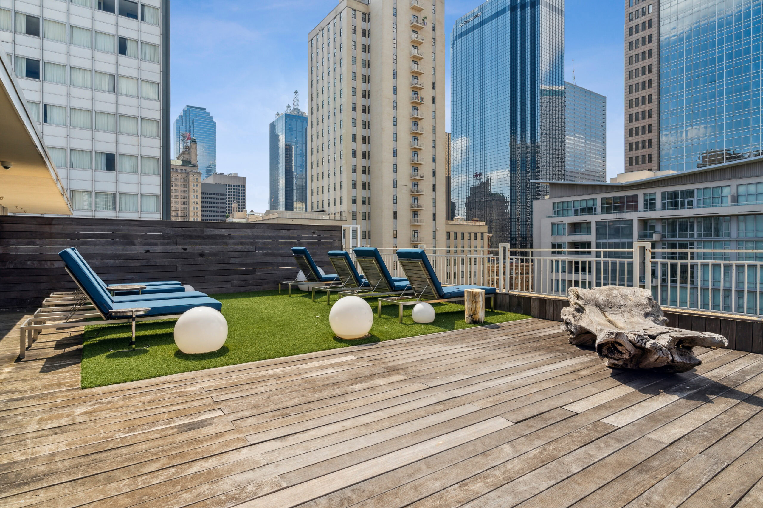 Outdoor patio with faux grass and lounge chairs next to spherical light fixtures on the floow with a view of the city at The Mercs apartments in Dallas Texas