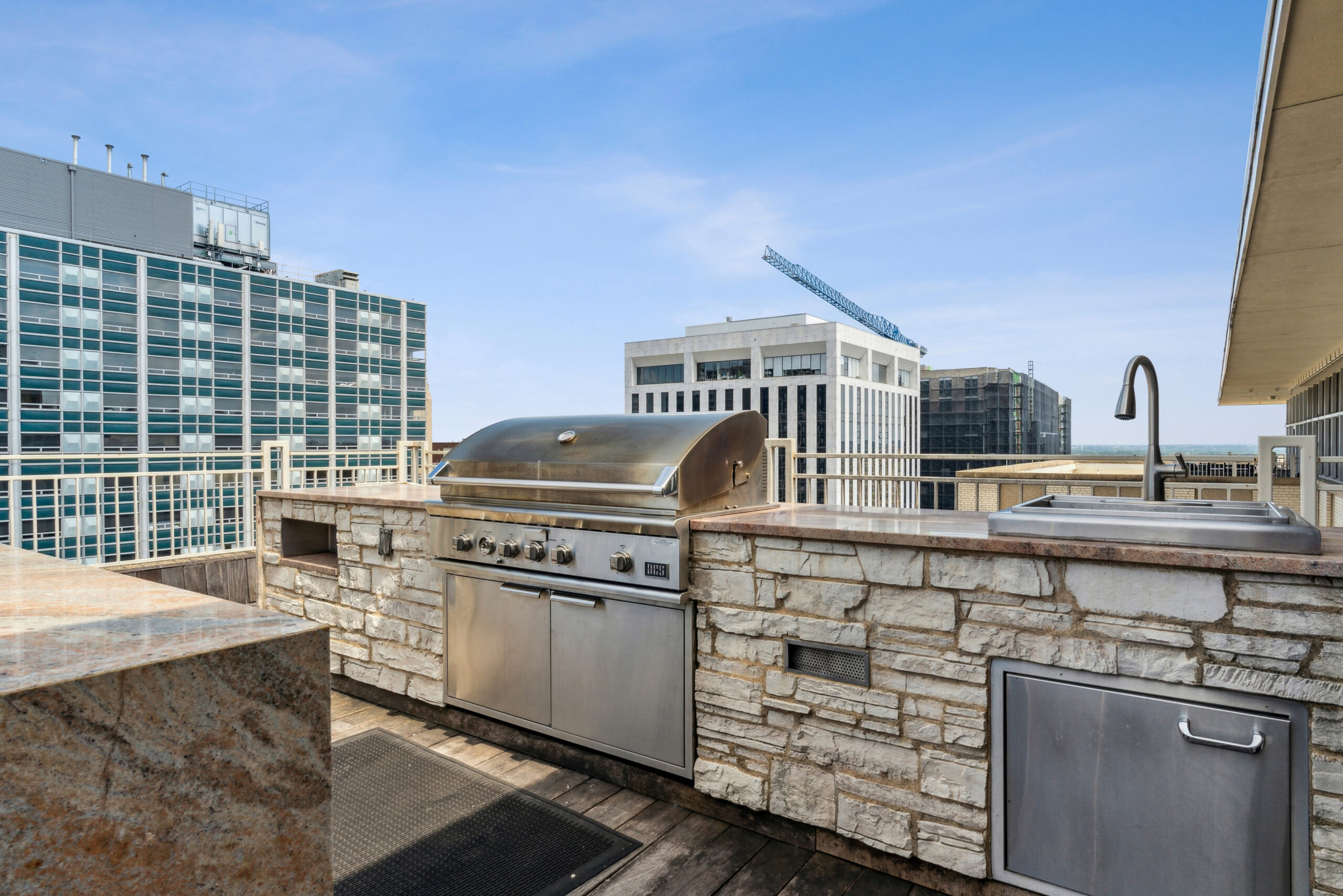 Outdoor grill, oven and stone wall kitchen area with a view of the city skyline at The Merc apartments in Dallas, Texas