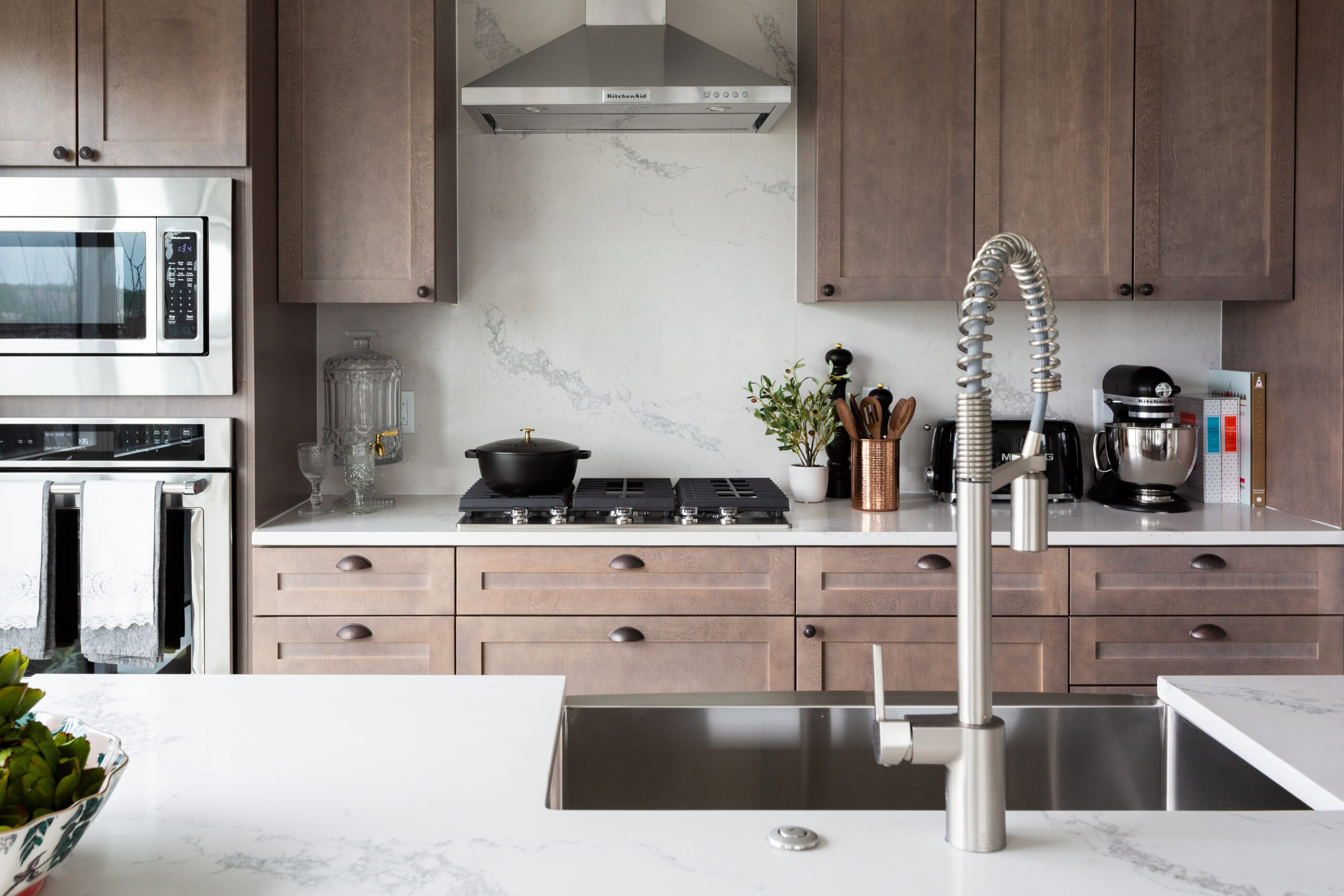 modern apartment kitchen with stainless steel apliances, marble backsplash and light brown cabinets