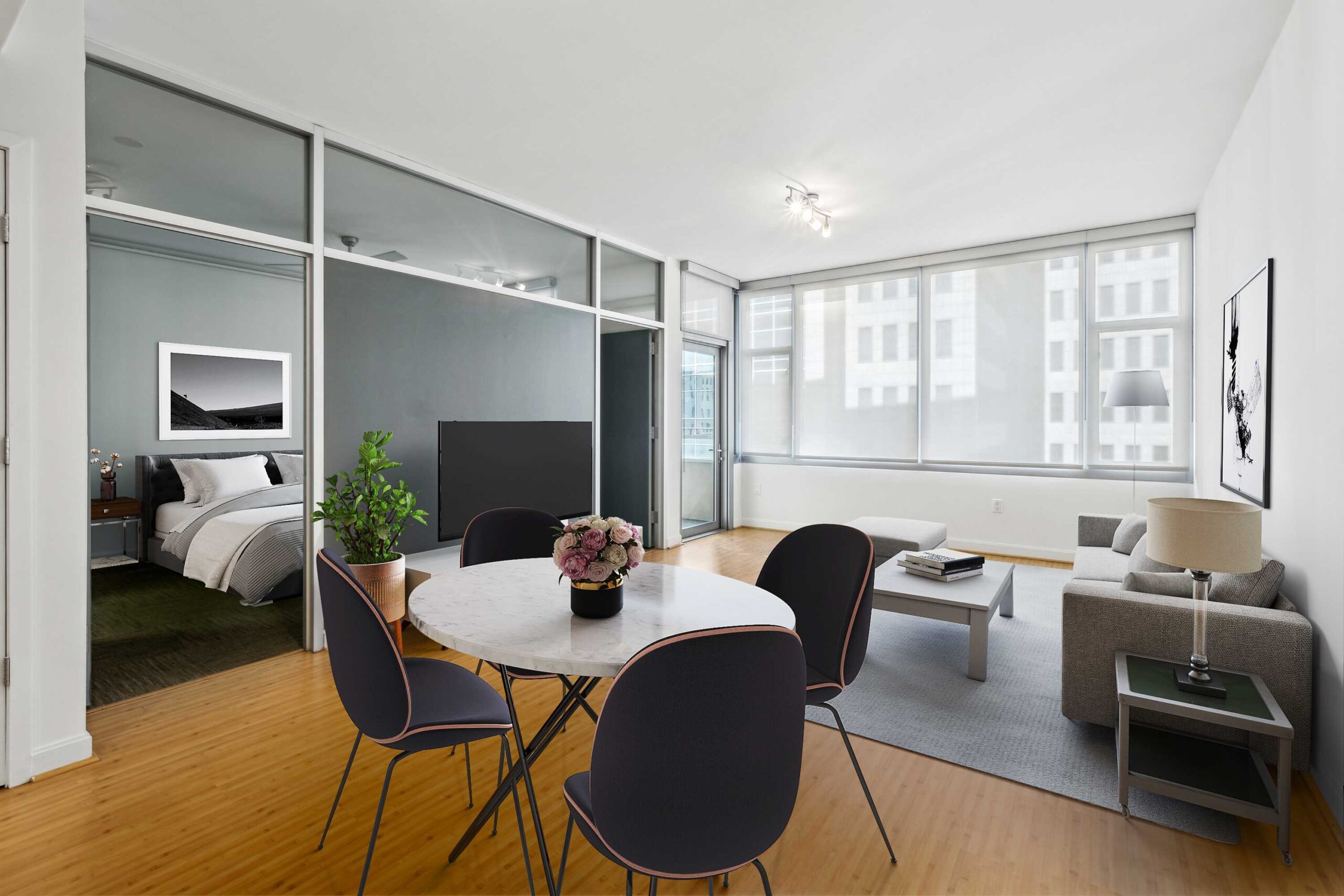 A modern apartment dining room area leading into its living room and facing a bedroom, with a large window at The Elements luxury apartments in Dallas Texas