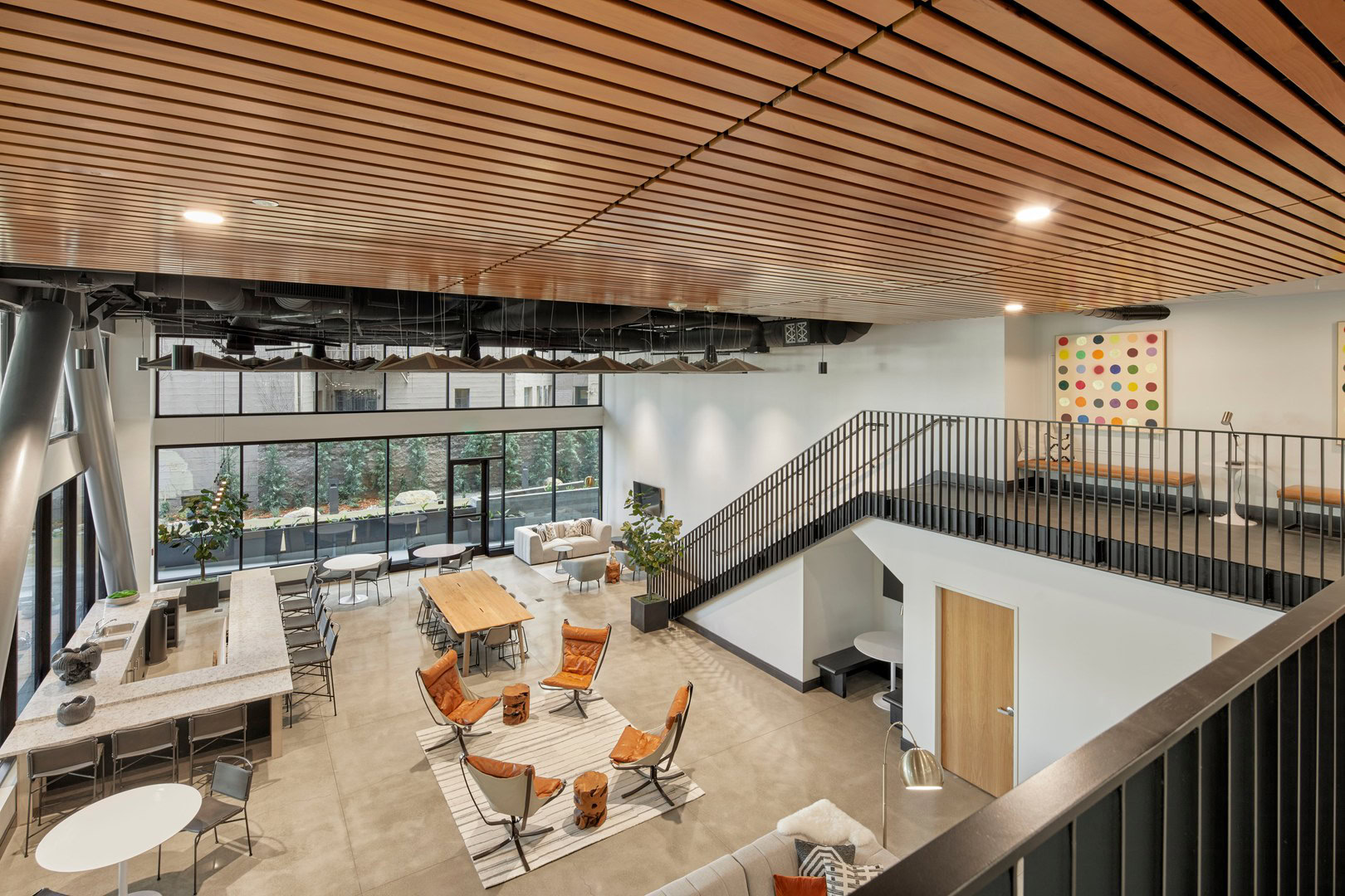 A spacious two level coworking space with lounging chairs, and a U shaped island for dining and entertaining at The Logan luxury apartments in Temescal CA