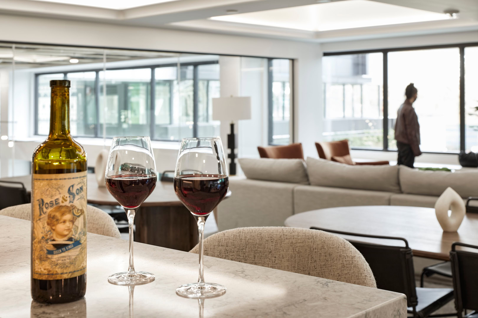 A bottle and two glasses of wine in a lounge with large windows bringing in natural lighting at The Logan luxury apartments in Oakland CA