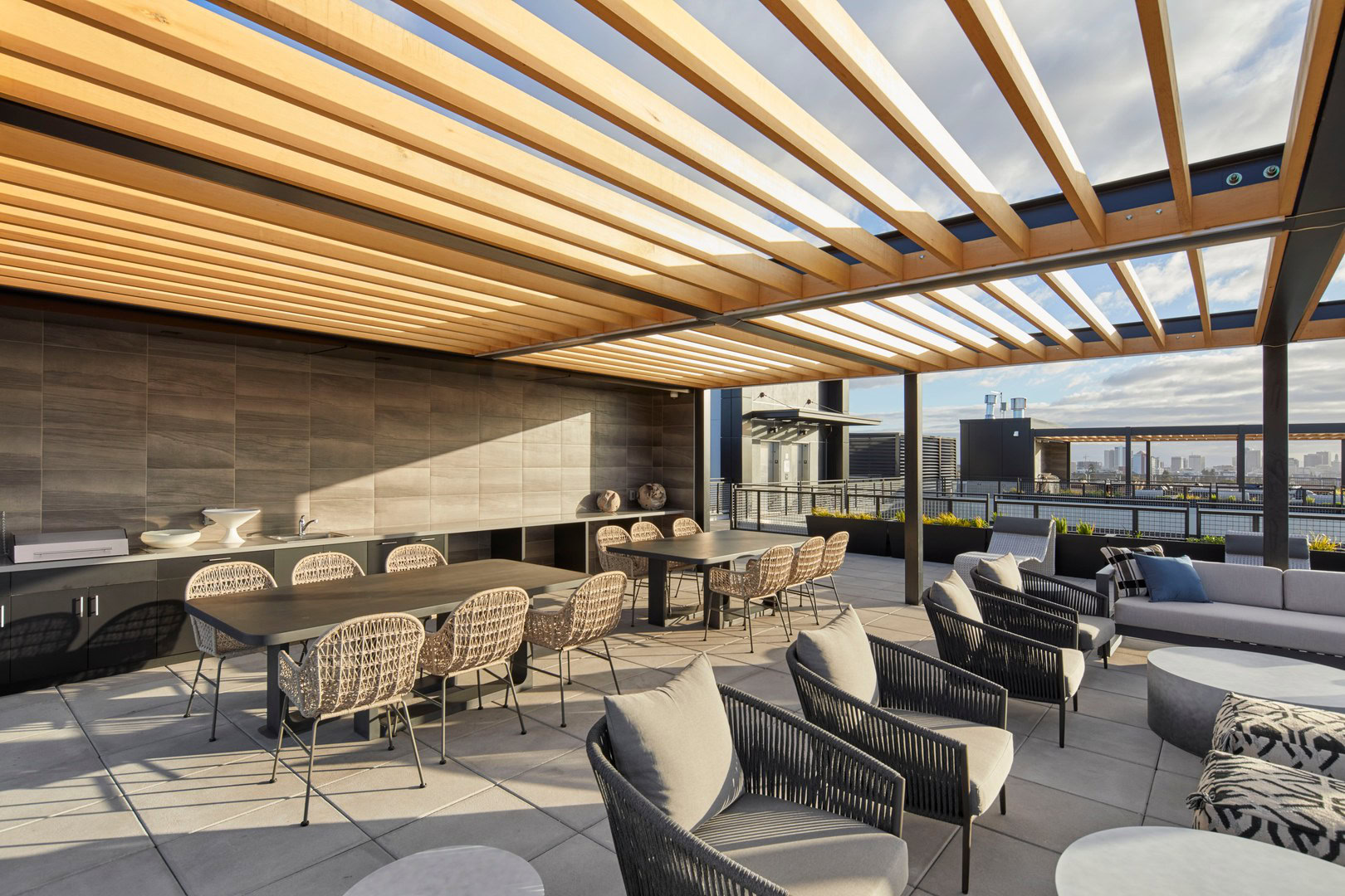 A rooftop lounge with pergola shading, outdoor grilling stations and dining tables in Oakland luxury apartments for rent at The Logan