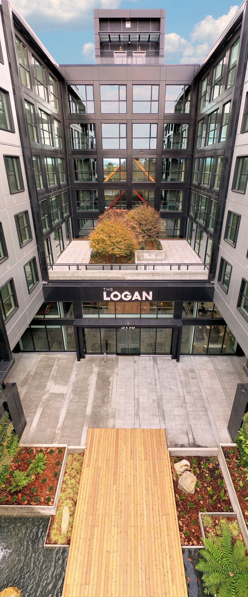 An entrance with biophilic elements including a wooden bridge surrounded by greenery and water feature in Temescal apartments, The Logan