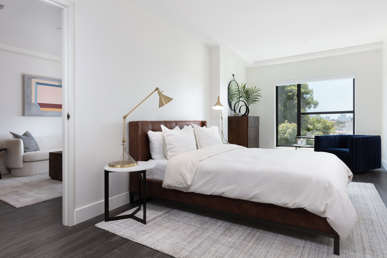A bedroom with a large window, wood flooring and a a door facing the living at The Logan apartments in Oakland CA