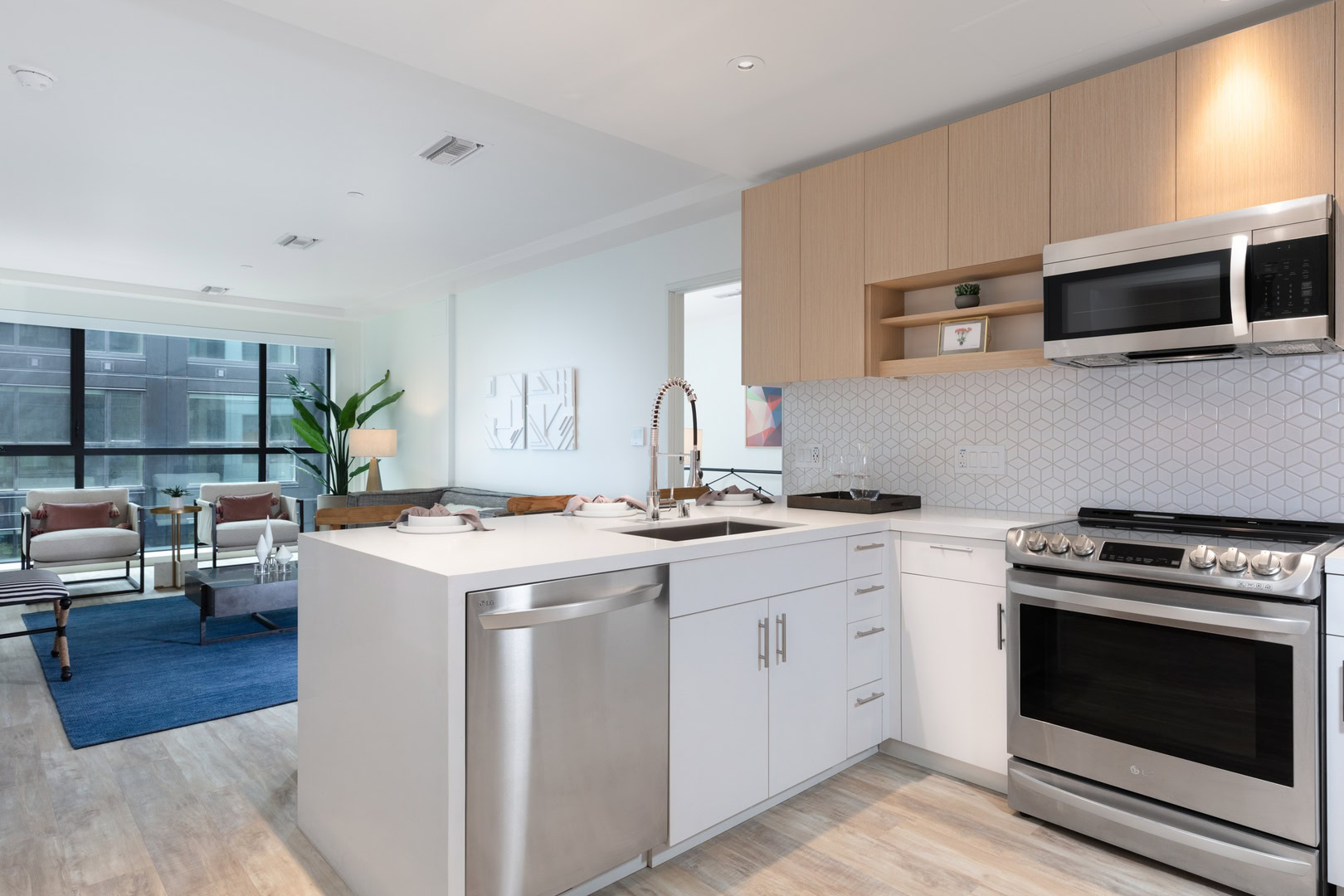 A modern kitchen with a peninsula, facing the living room with a floor to ceiling window in the Logan apartments in temescal oakland.