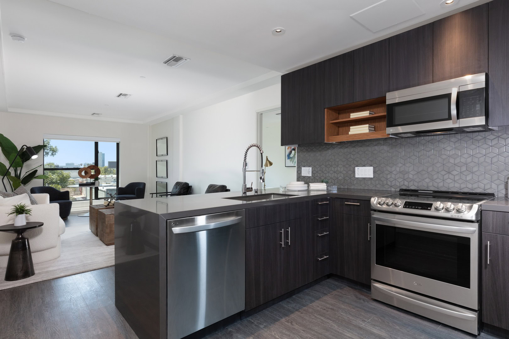 A peninsula kitchen with dark wood cabinets facing a spacious living room at The Logan temescal oakland ca apartments