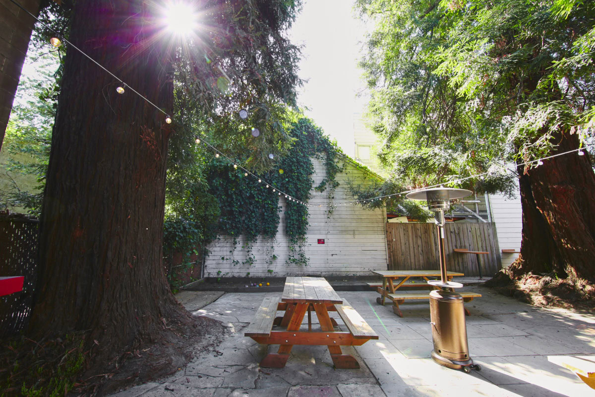 A restaurants back patio with picnic tables and fairy lights in a neighborhood near The Logan, apartments in Temescal