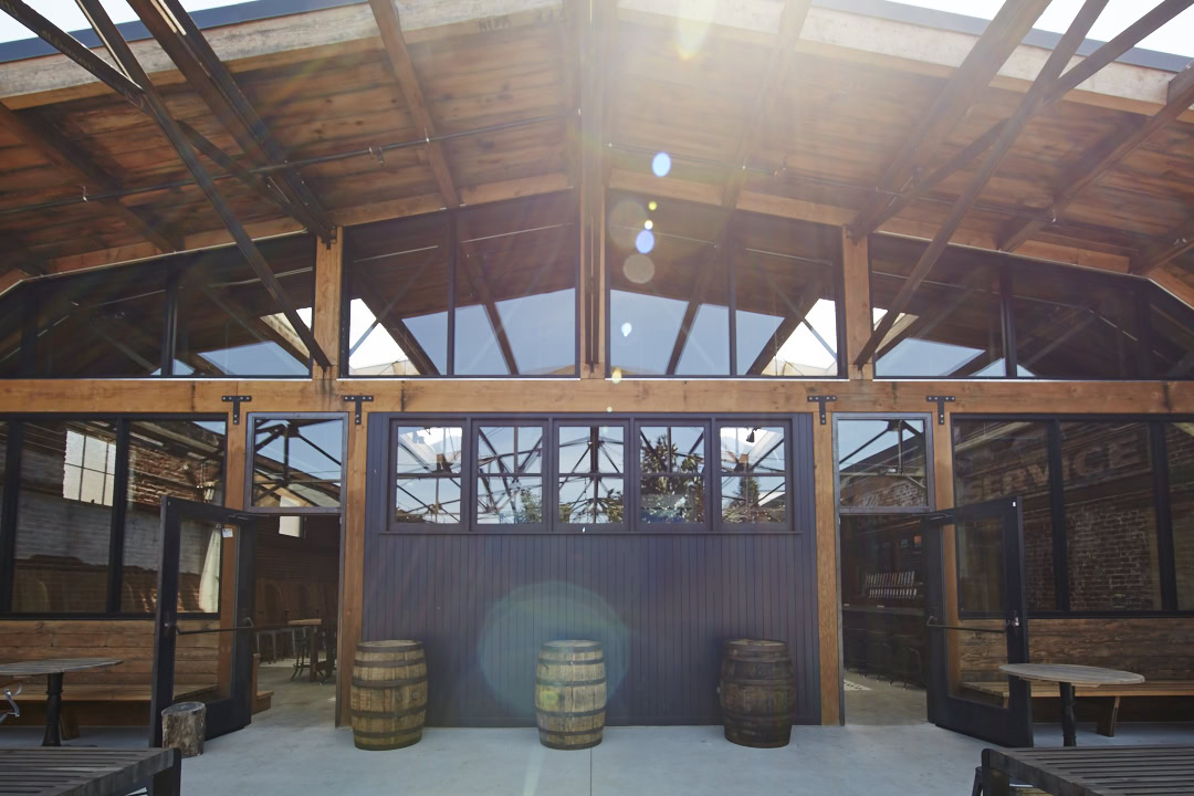 A rustic, farm style restaurant with outdoor seating and barrels for decoration by the entrance to indoor seating in a neighborhood near The Logan, apartments in Temescal CA