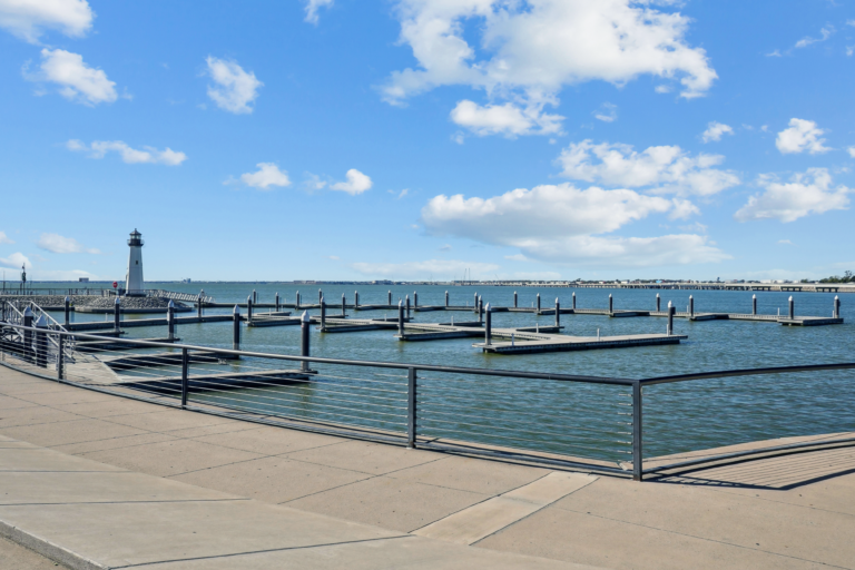 A serene harbor scene with empty docks and a lighthouse on the left under a bright blue sky with fluffy clouds, evoking a calm and peaceful mood.