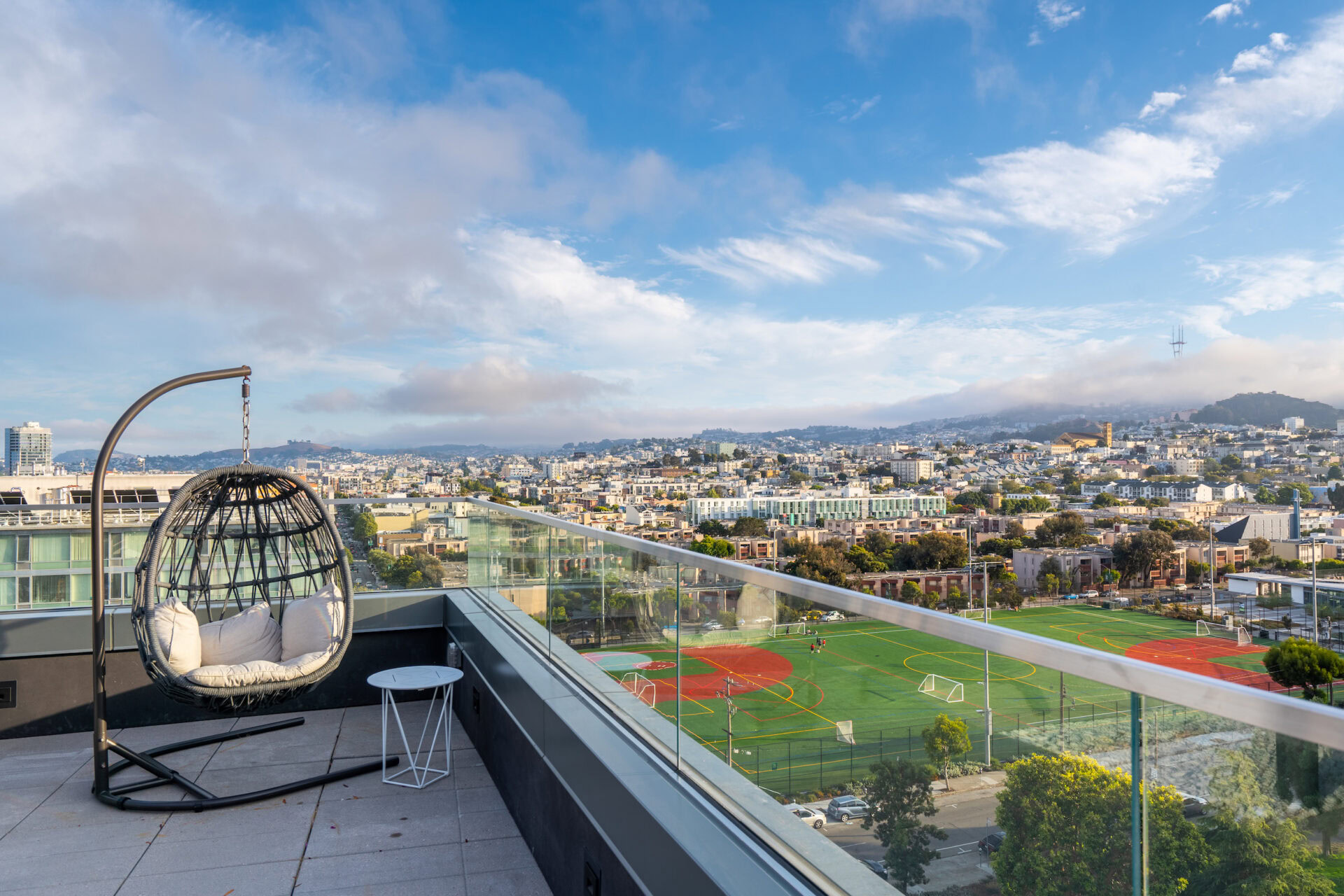 Rooftop terrace with stylish hanging chair and panoramic city views, featuring a glass railing and outdoor seating area, perfect for relaxation and enjoying urban scenery.